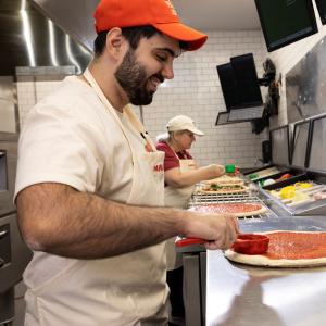 Papa Johns team member spreading sauce on pizza