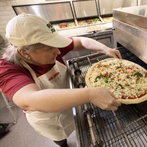 Papa Johns team member placing pizza inside oven