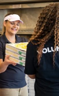 A Papa Johns team members hands surplus pizza orders to a volunteer.